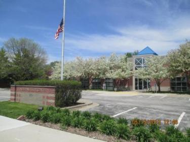 Bondurant City Hall building with a brick exterior, blooming trees in front, and an American flag flying on a tall flagpole near the entrance.