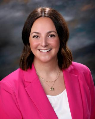 Headshot of Assistant Director Megan Sockness Teeple in a Pink Blazer with a grey background